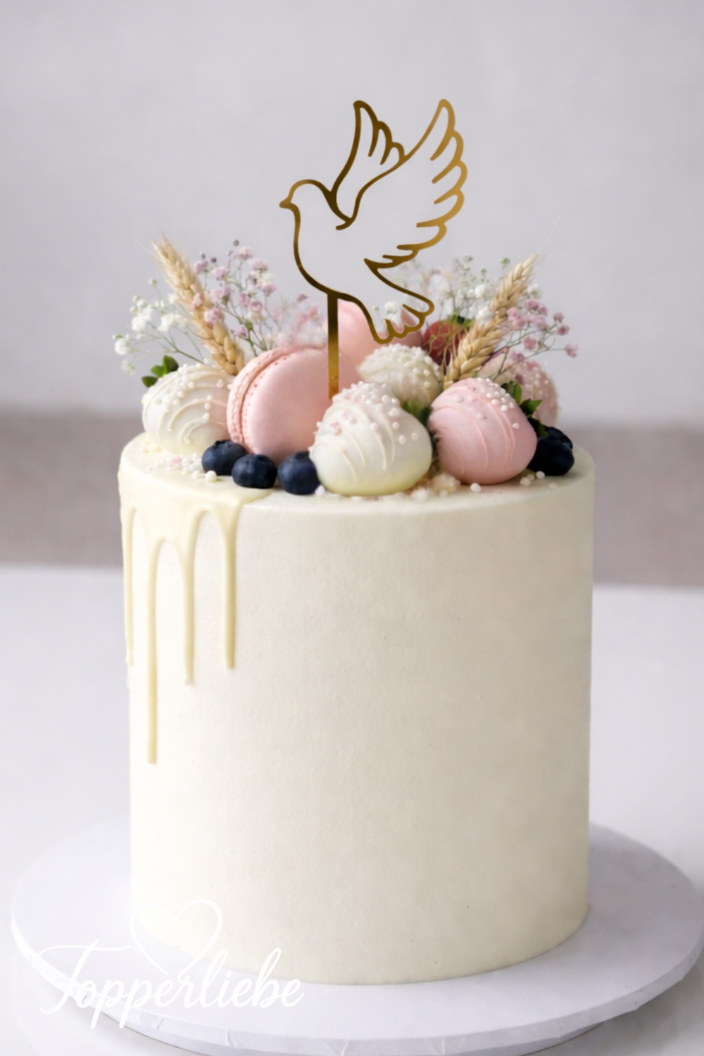 Kommunionstorte in Weiß mit goldener Tauben-Silhouette als Cake Topper, dekoriert mit Macarons, Beeren und zartem Drip