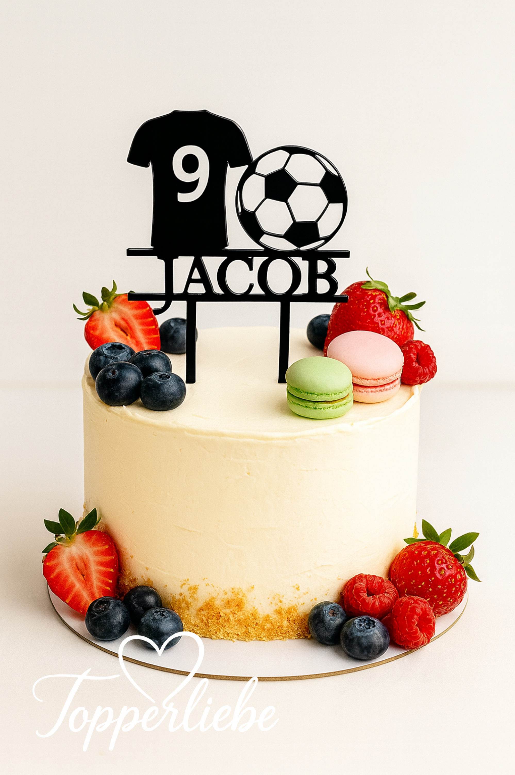 Personalisierter Fußball-Torten-Topper mit Name und Zahl in Form eines Trikots mit Ball auf einem hellen Geburtstagskuchen mit Früchten.