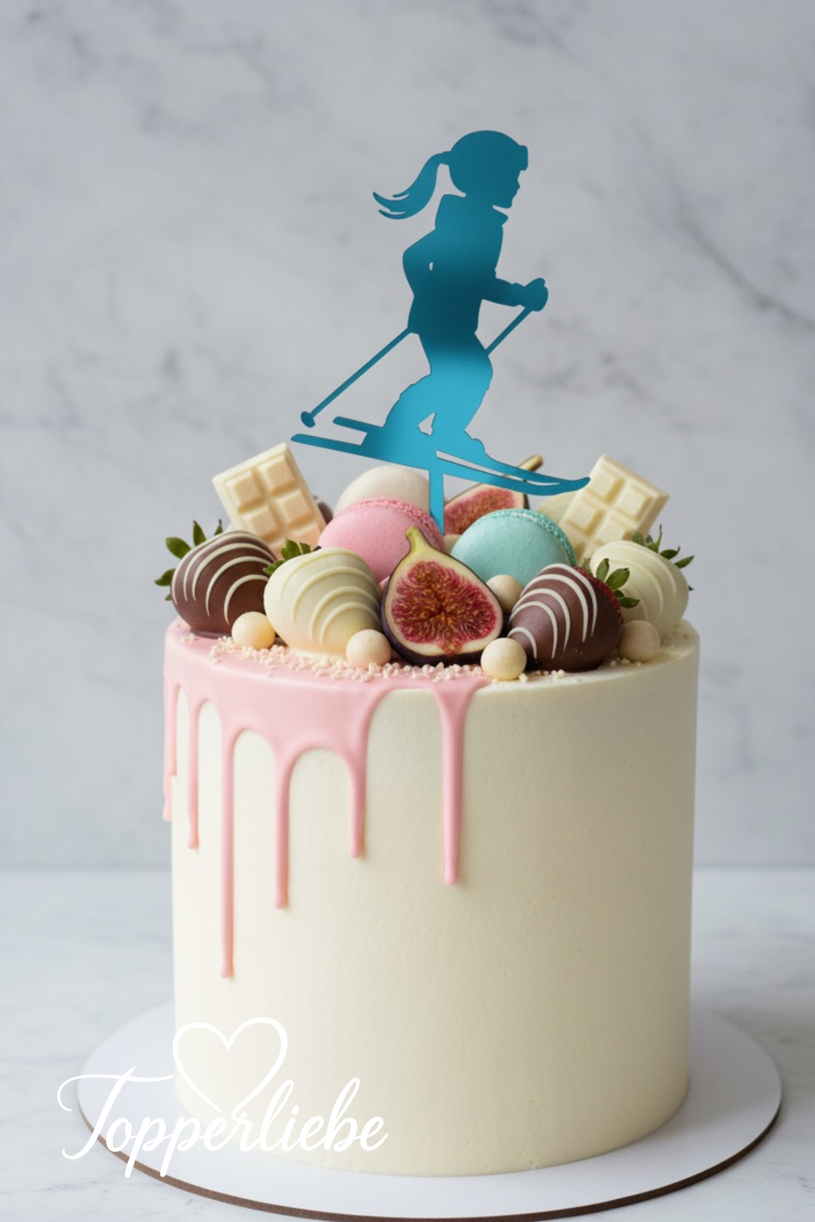 Weißer Kuchen mit rosa Drip und hellblauem Torten Topper – Mädchen auf Skiern, dekoriert mit Schokolade, Feigen und Makronen, ideal für Kindergeburtstage oder Wintersportfans