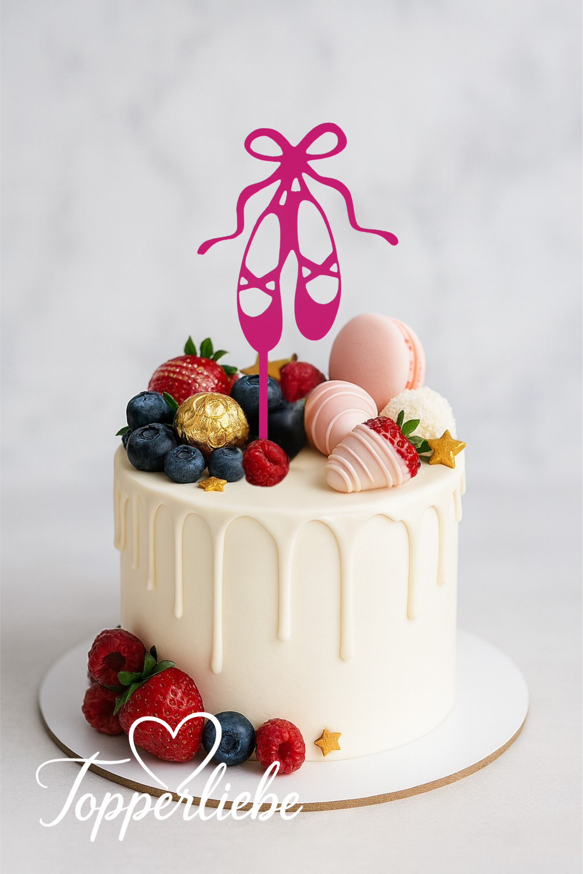 Elegante einstöckige weiße Torte mit einem modernen Acryl-Topper in Form von Ballettschuhen in Pink, dekoriert mit Macarons, Beeren und goldenen Details auf hellgrauem marmoriertem Hintergrund.