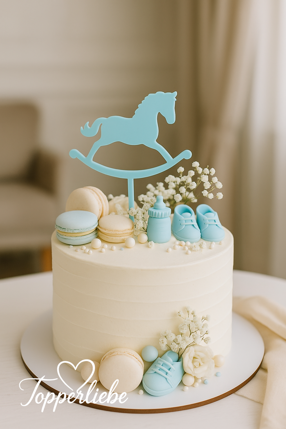 Weißer Baby Shower Tort mit hellblauem Schaukelpferd-Topper, dekoriert mit Macarons, Babyschuhen und Schleierkraut – elegante Deko im Pastellstil.
