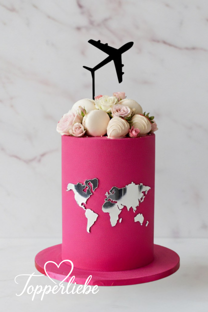 Rosa Kuchen mit silberner Weltkarte und schwarzem Flugzeug Torten Topper – moderne Reisedeko mit Blumen und Meringues, ideal für Weltenbummler