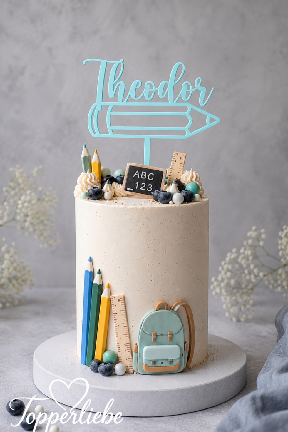 Personalisierter blauer Tortentopper zur Einschulung mit dem Namen Theodor und Buntstift-Motiv auf einer dekorierten Einschulungstorte.